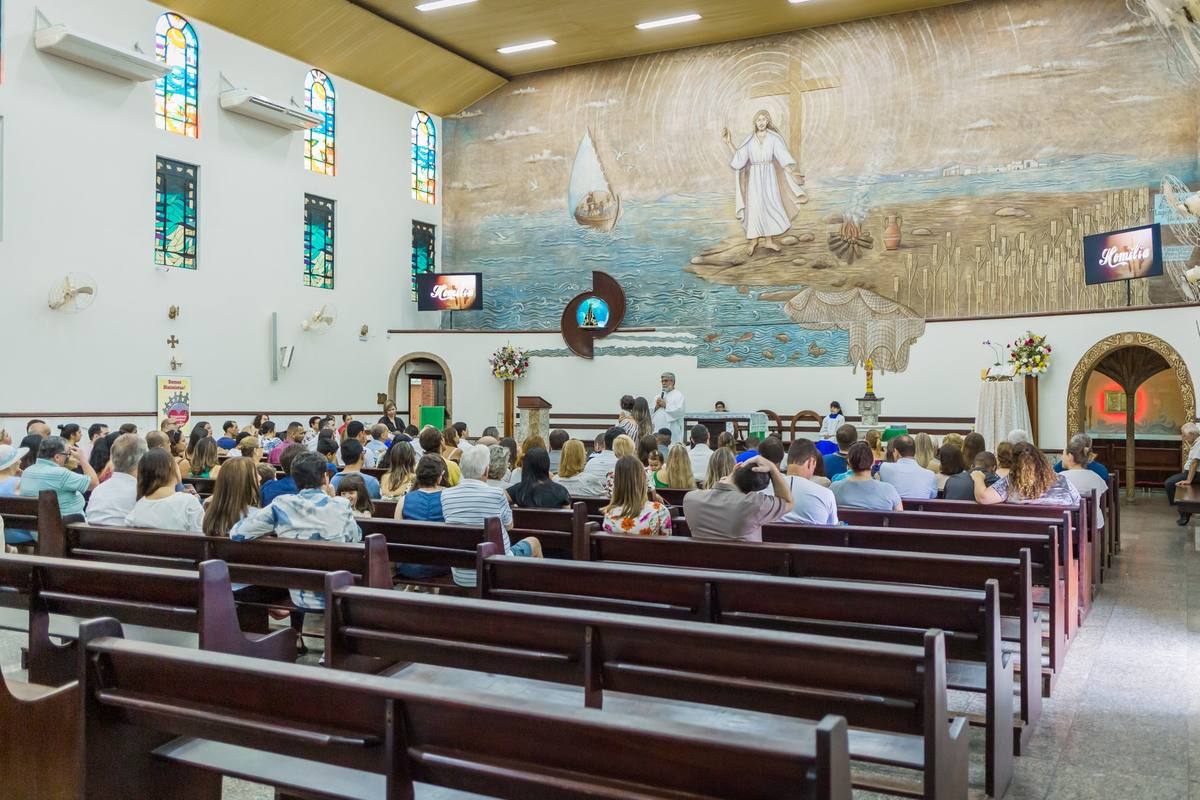 Interior da Igreja Matriz com fiéis nos bancos e o grande painel em baixo relevo no presbitério