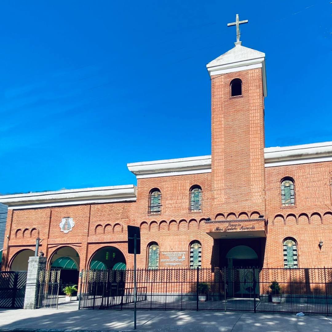 Fachada de tijolos aparentes da Igreja Matriz Nossa Senhora Aparecida, com torre e cruz, sob céu azul